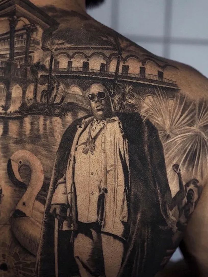 Tattoo of rich man standing in front of water and a mansion