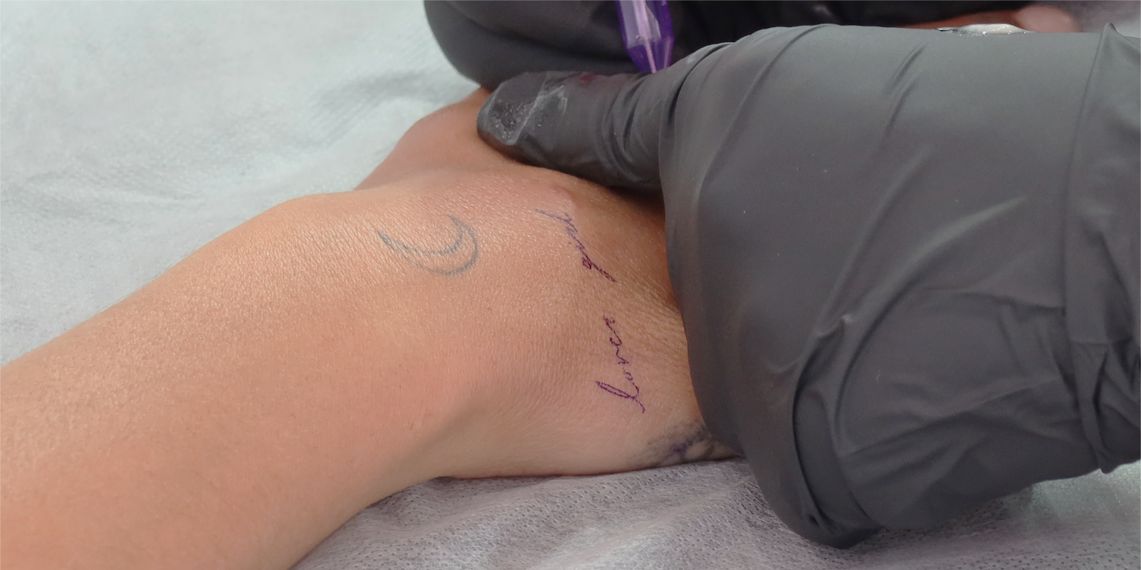 Cresent moon tattoo with cursive writing underneath on the back of a hand