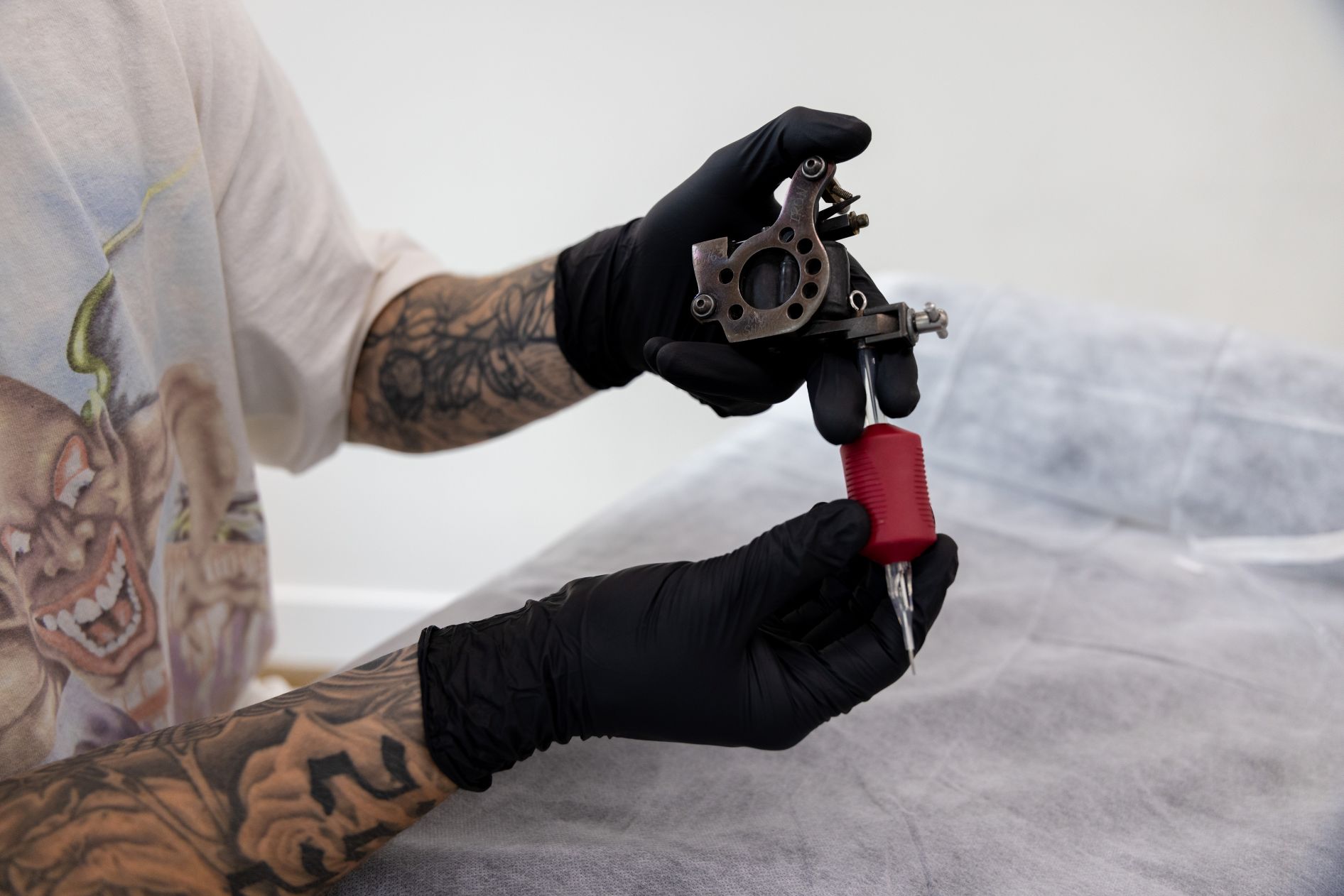 a person with tattooed arms holding a tattoo gun in gloved hands