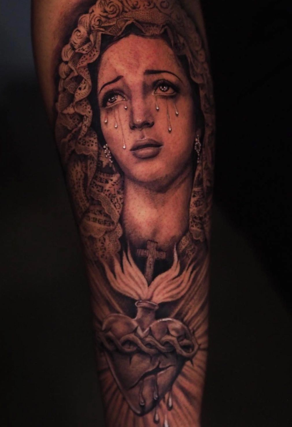Realistic black and grey religious sleeve tattoo featuring a crying Madonna
